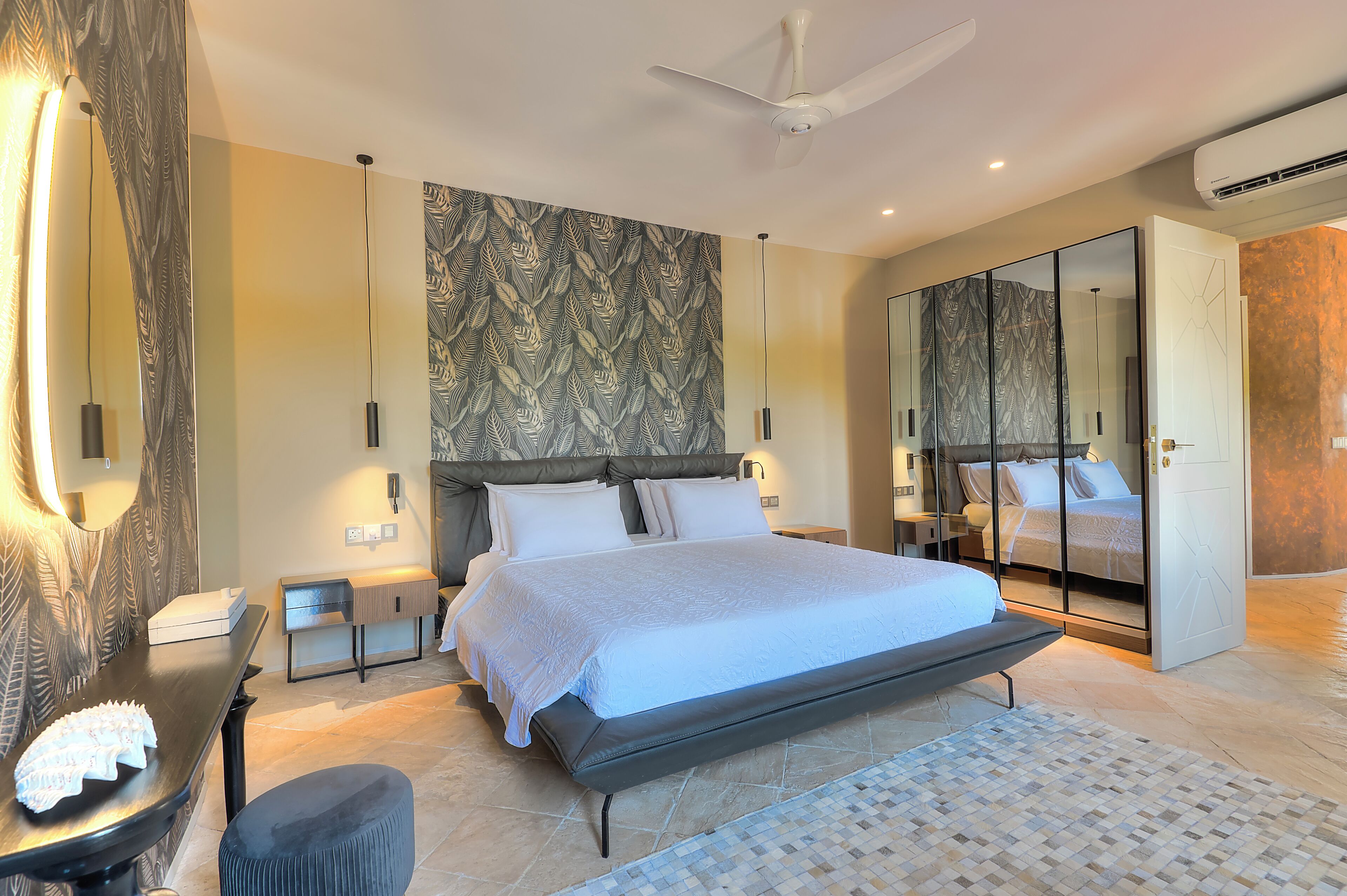Une chambre moderne avec un grand lit, une armoire avec un miroir, une table de chevet et un ventilateur de plafond.