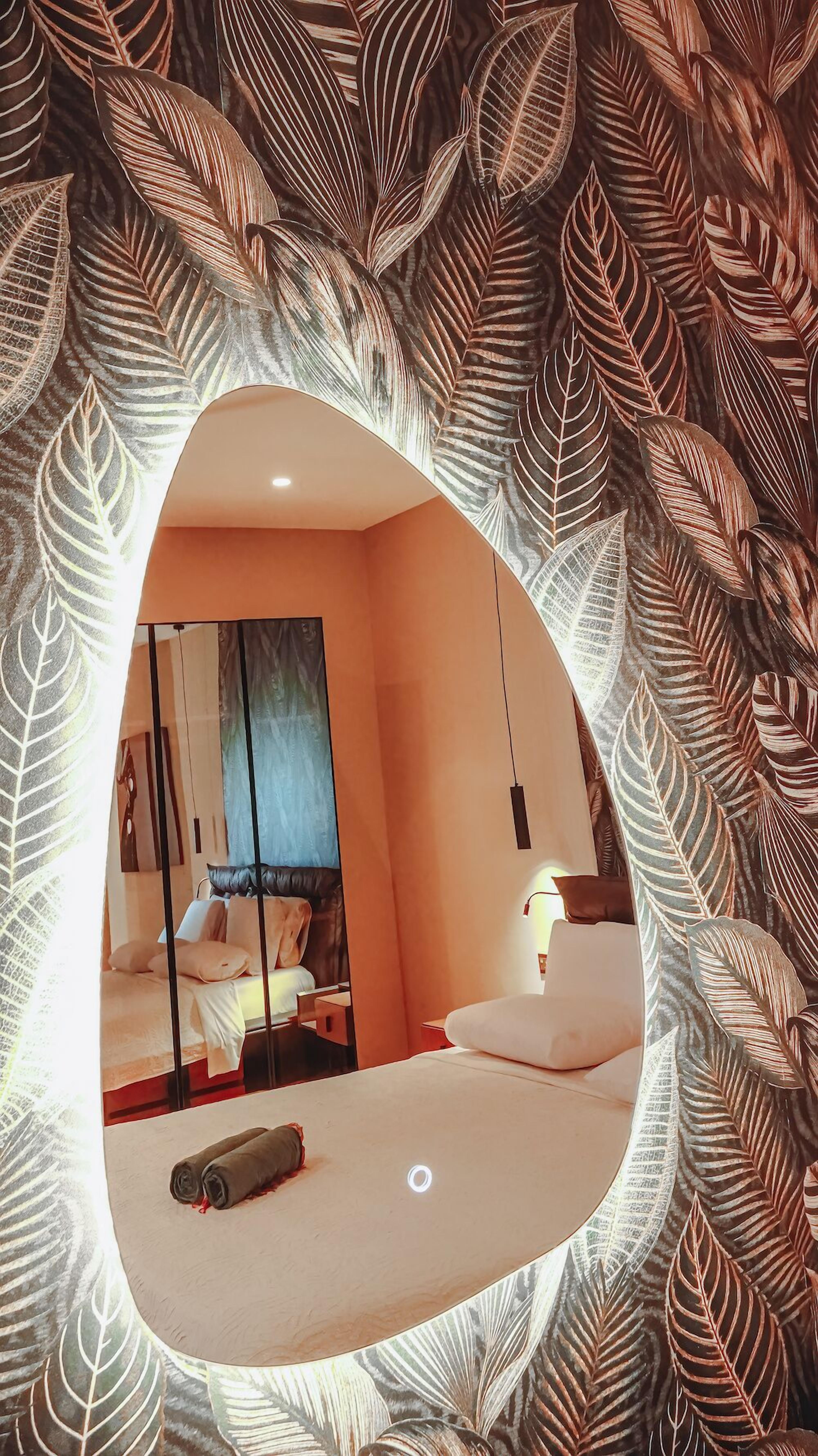 A bedroom with a bed, a bedside table, a mirror, and a window.