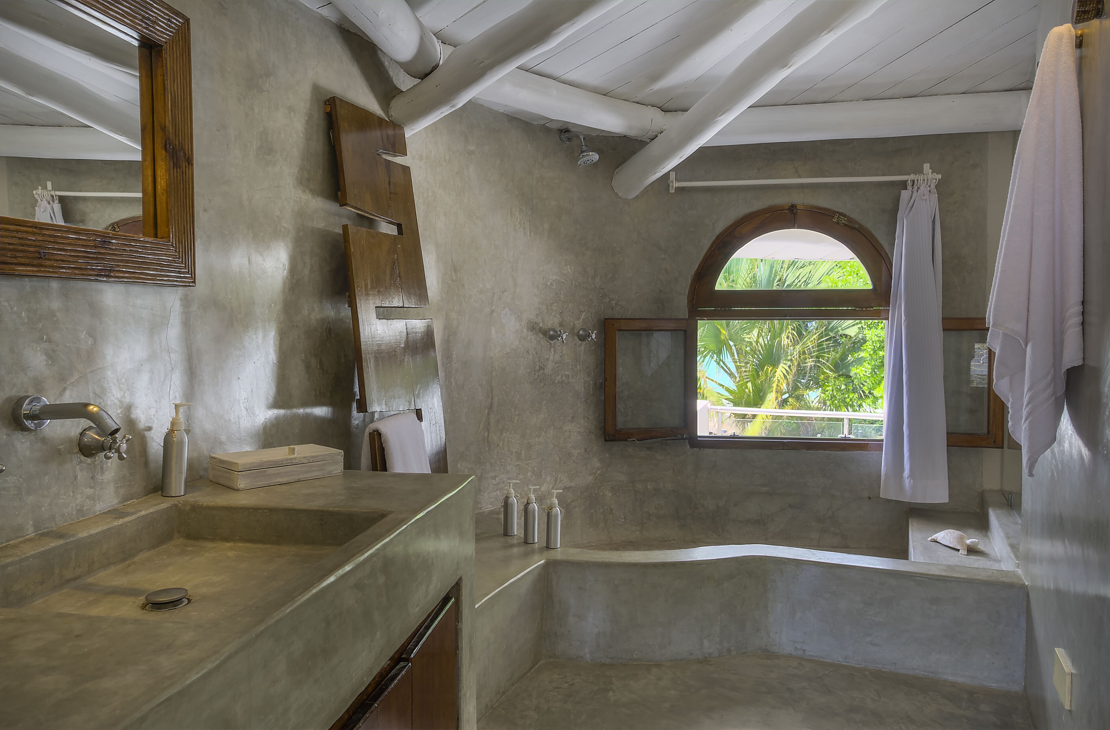 A bathroom with a large bathtub, a sink with a mirror, and a window with a view of greenery.