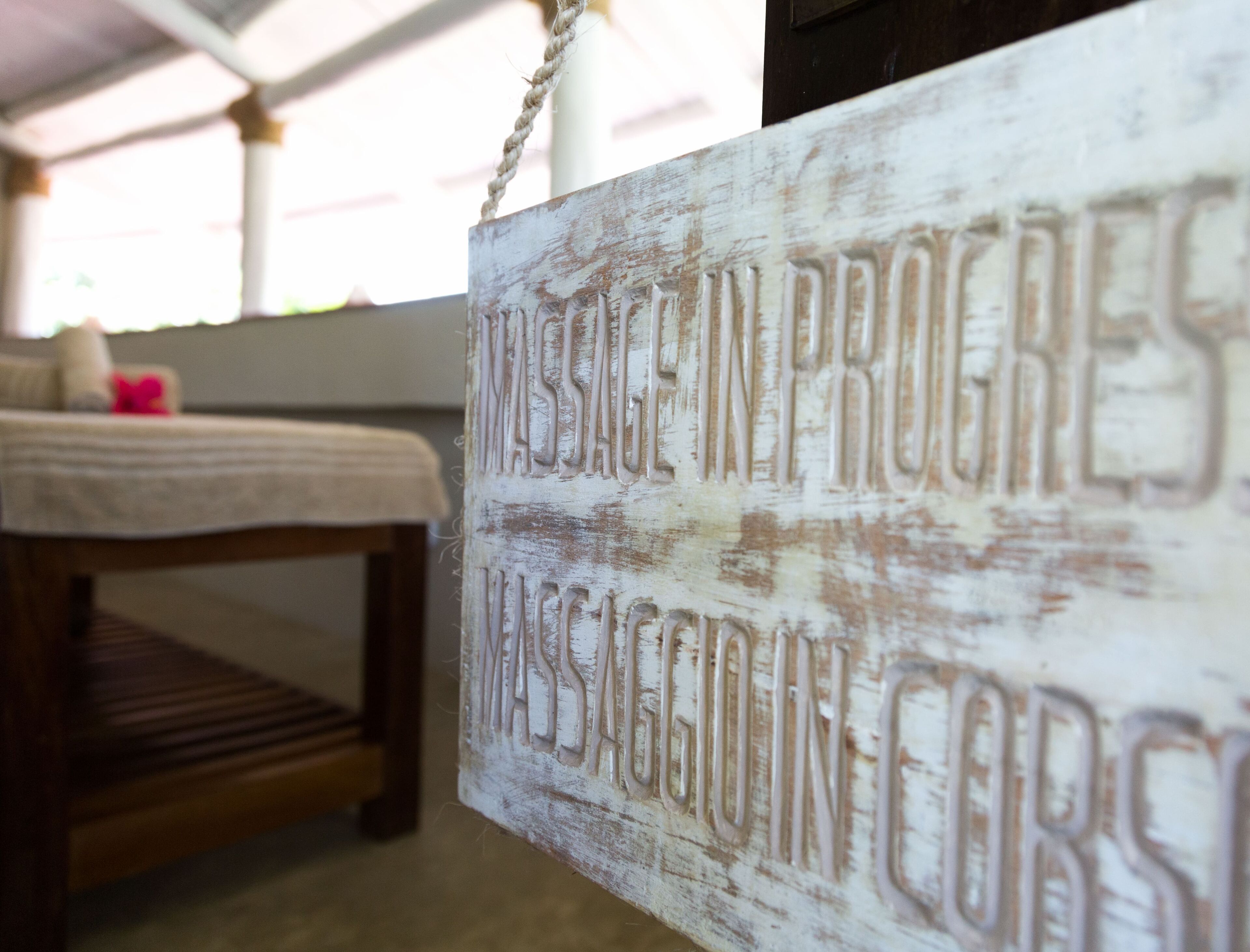 A rustic wooden sign with the text "MASSEAGE IN PROGRES MASSAGE IN CORS".