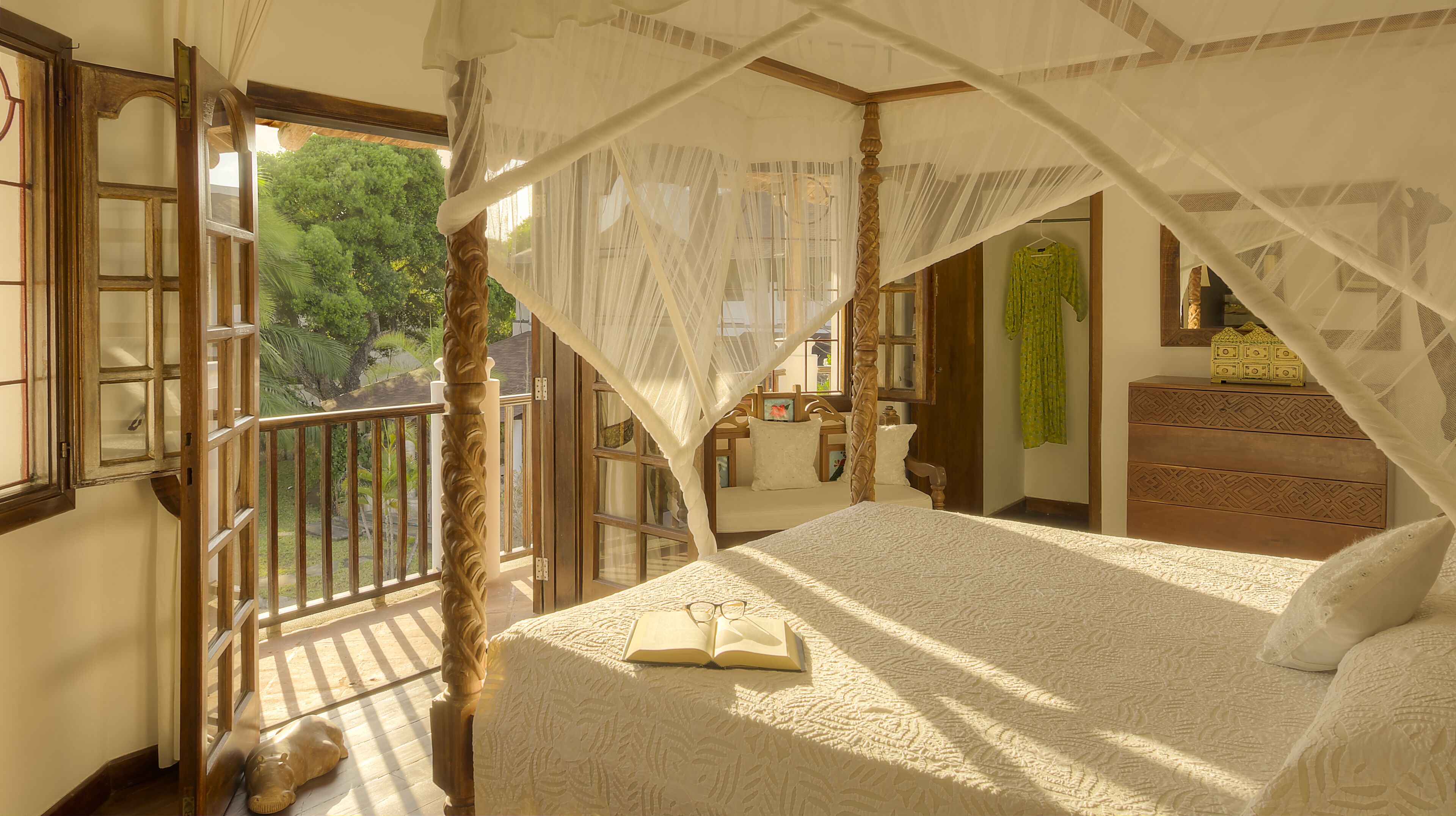 A bedroom with a canopy bed, a view of the outdoors, and a wooden headboard.