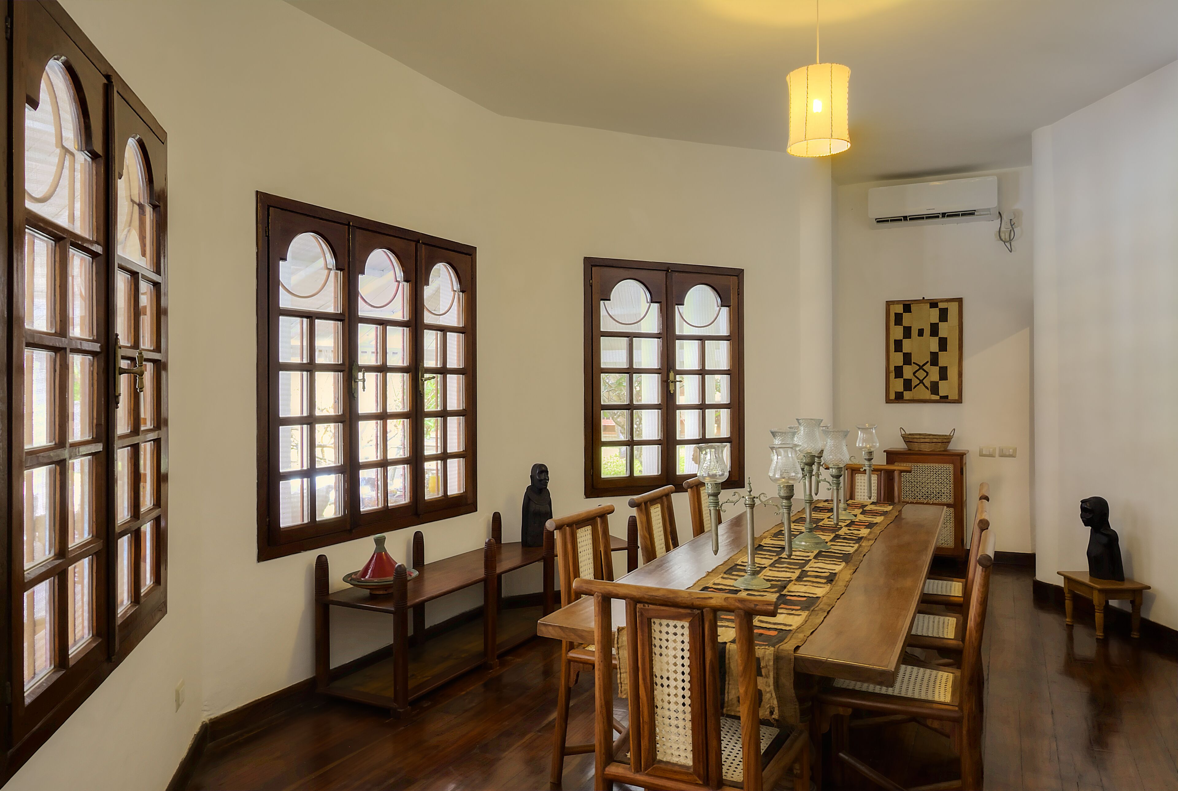 Un comedor con una larga mesa de madera, varias sillas y ventanas grandes con vidrieras decorativas.