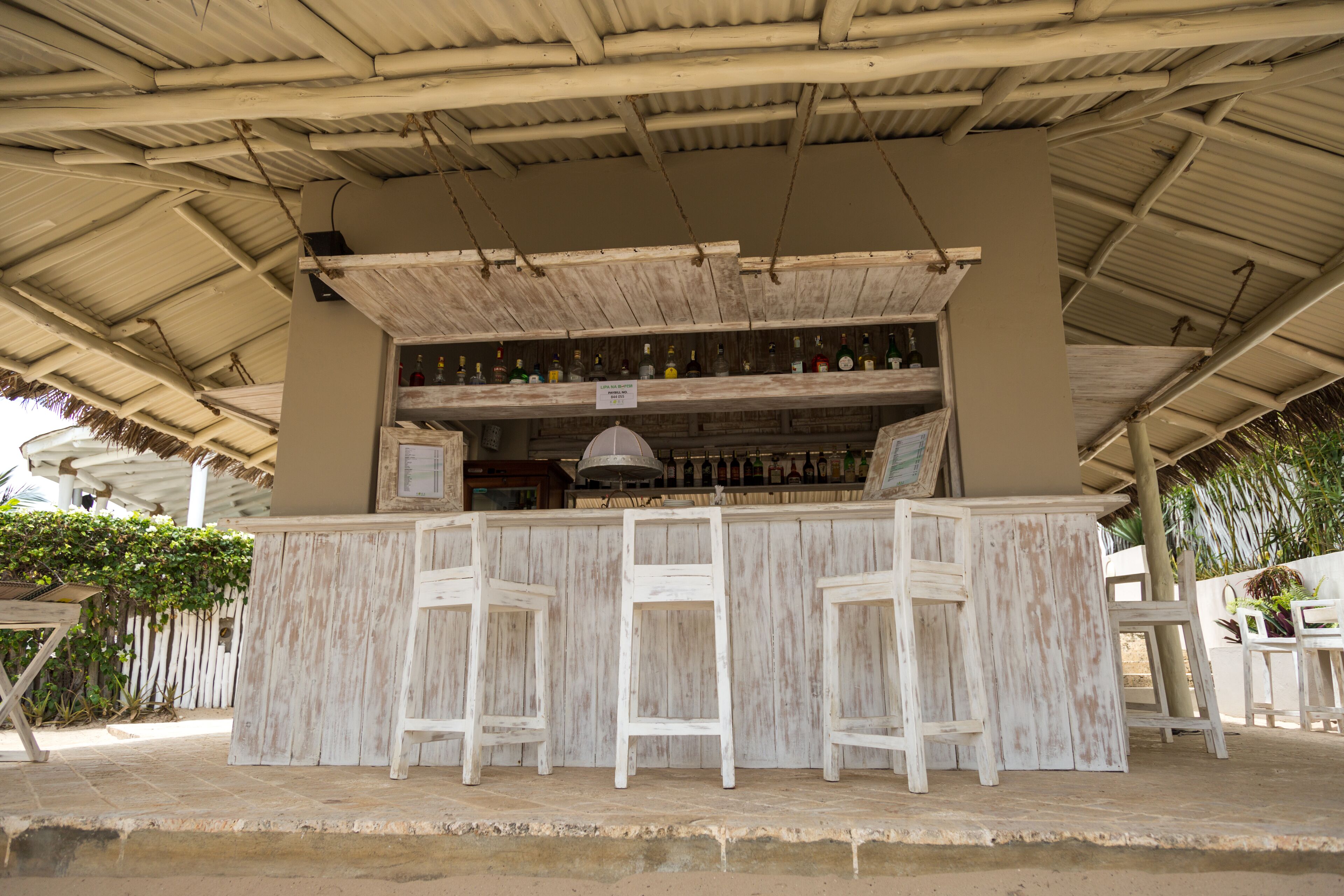 Una zona de bar con una barra de madera rústica, dos taburetes blancos y una campana de metal.