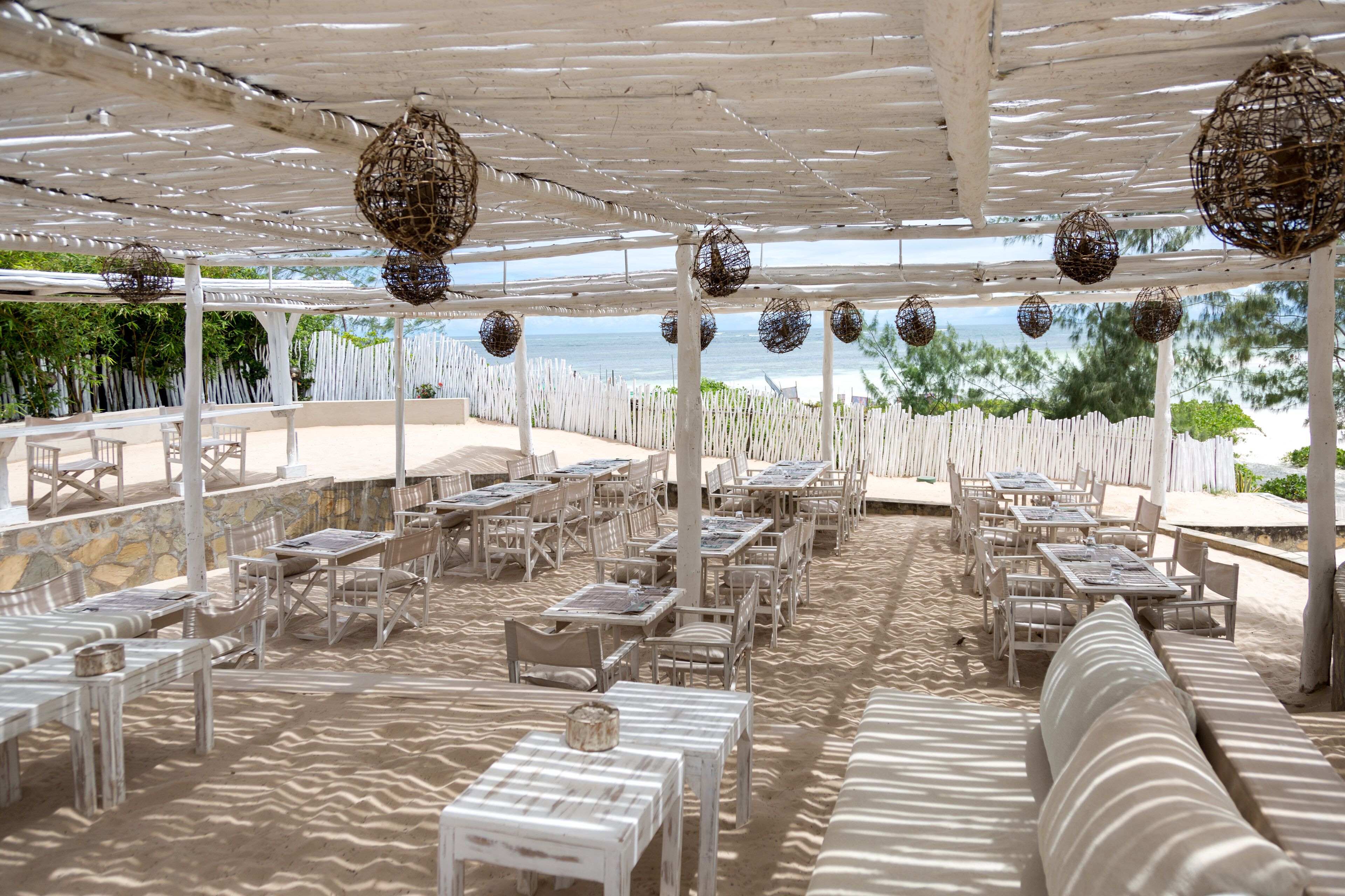 An outdoor dining area with white tables and chairs, a white pergola, and hanging decorative spheres.