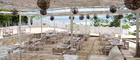An outdoor dining area with white tables and chairs, a white pergola, and hanging decorative spheres.
