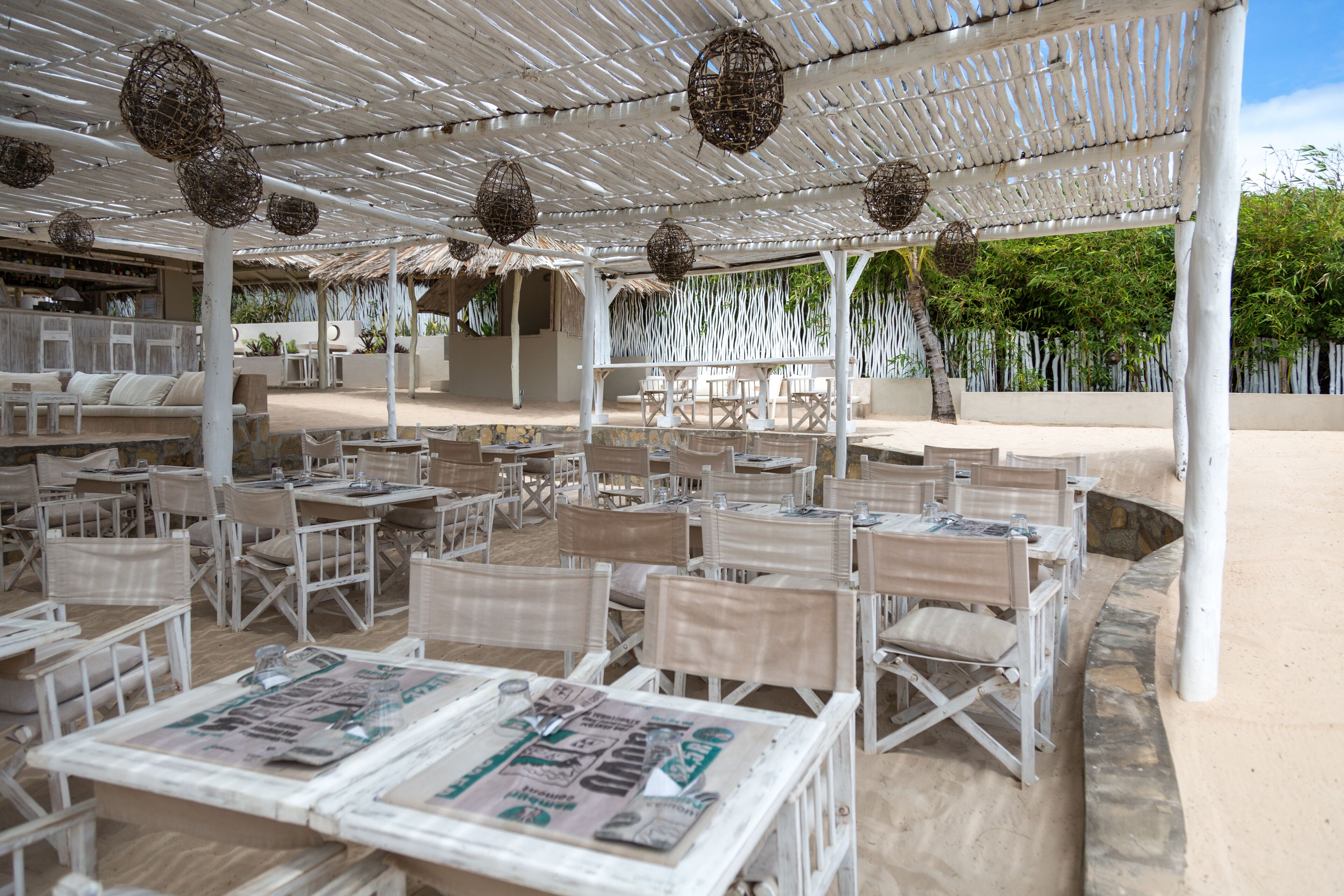 An outdoor seating area with white wicker furniture and a thatched roof structure.