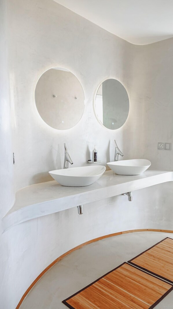 Un baño moderno con dos lavamanos blancos, espejos redondos y un tapete de madera.