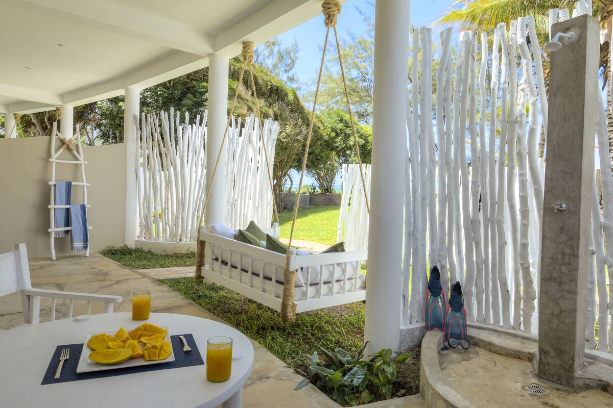 A covered outdoor seating area with a white table, a hanging chair, and a white fence.