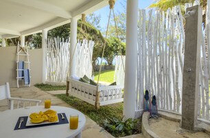 Un espacio de estar al aire libre cubierto con una mesa blanca, una silla colgante y una cerca blanca.