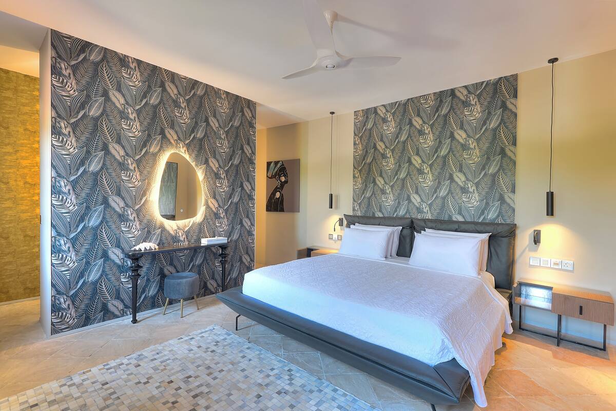A modern bedroom with a large bed, a vanity with a mirror, and patterned wallpaper.