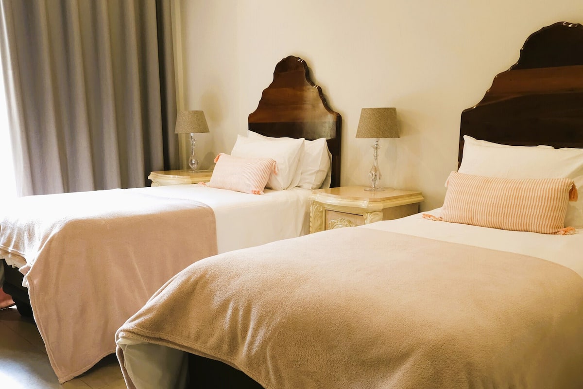 Une chambre d’hôtel avec deux lits, chacun doté d’une tête de lit en bois, de draps blancs et de lampes de chevet.