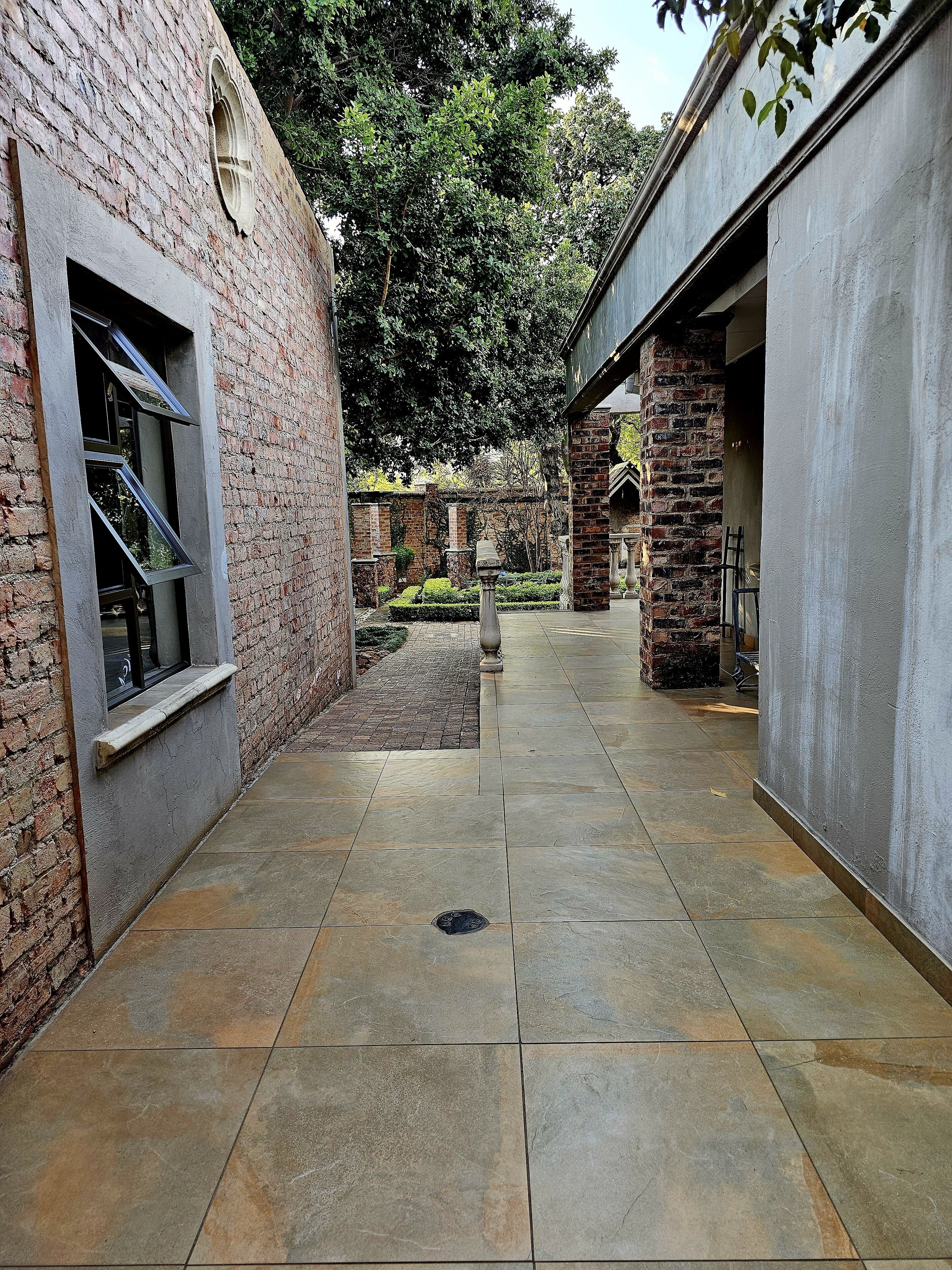 A courtyard with a brick wall, a tiled floor, and a small garden area.