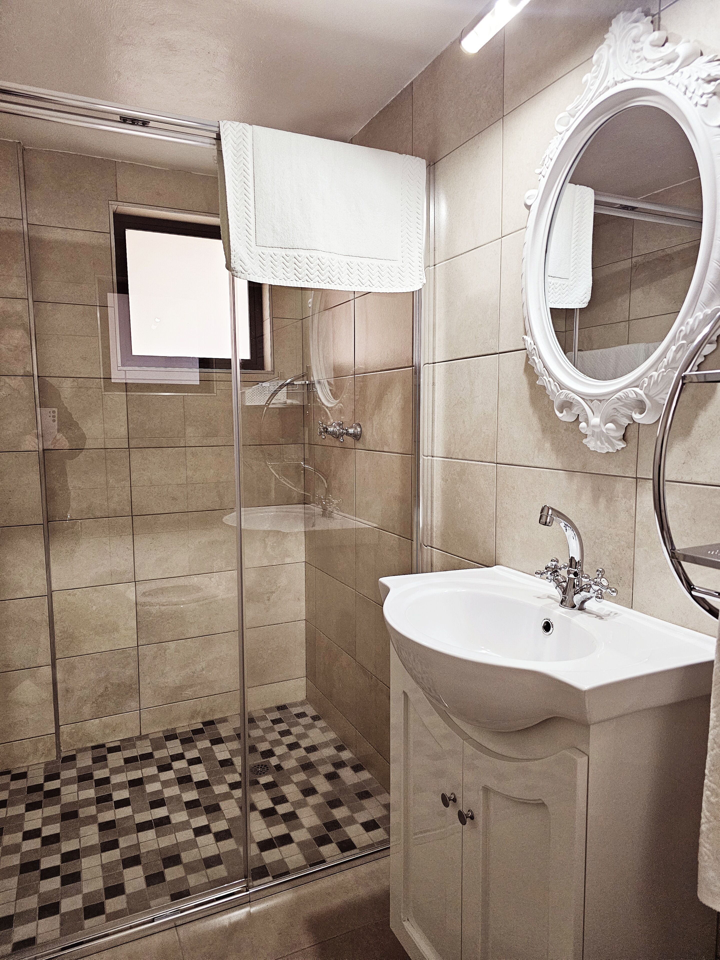 Un baño con ducha de vidrio, lavamanos blanco y espejo con marco decorativo.