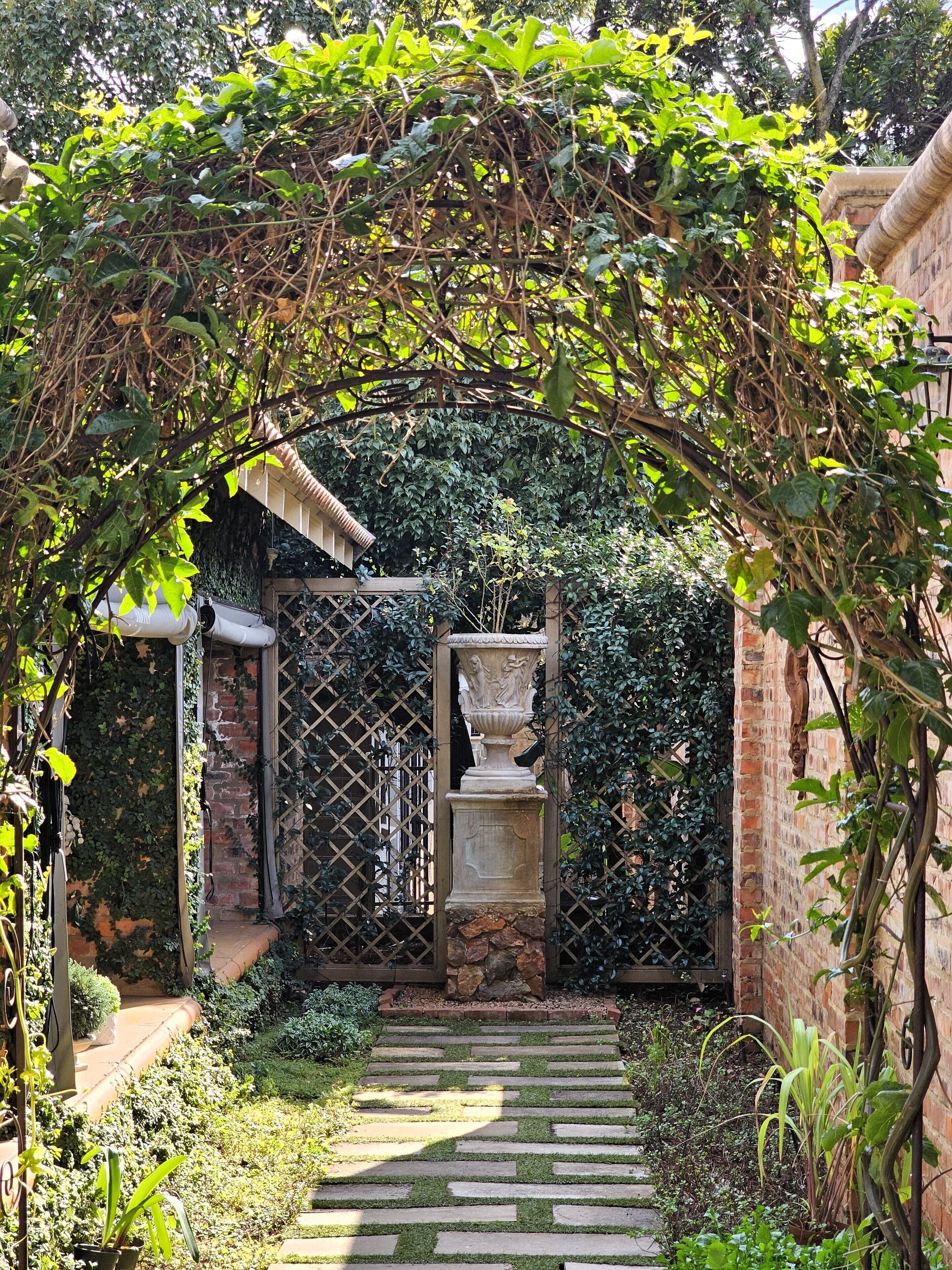A garden pathway leading to a brick wall with a decorative urn.