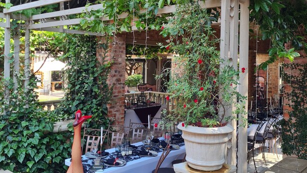 An outdoor dining area with a covered patio, tables set for dining, and a decorative flamingo statue. - Maison de Leo Luxury Guesthouse (Pretoria)