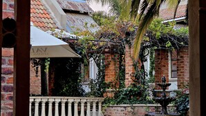 A pool area with a fountain, surrounded by a brick wall and greenery. - Maison de Leo Luxury Guesthouse (Pretoria)