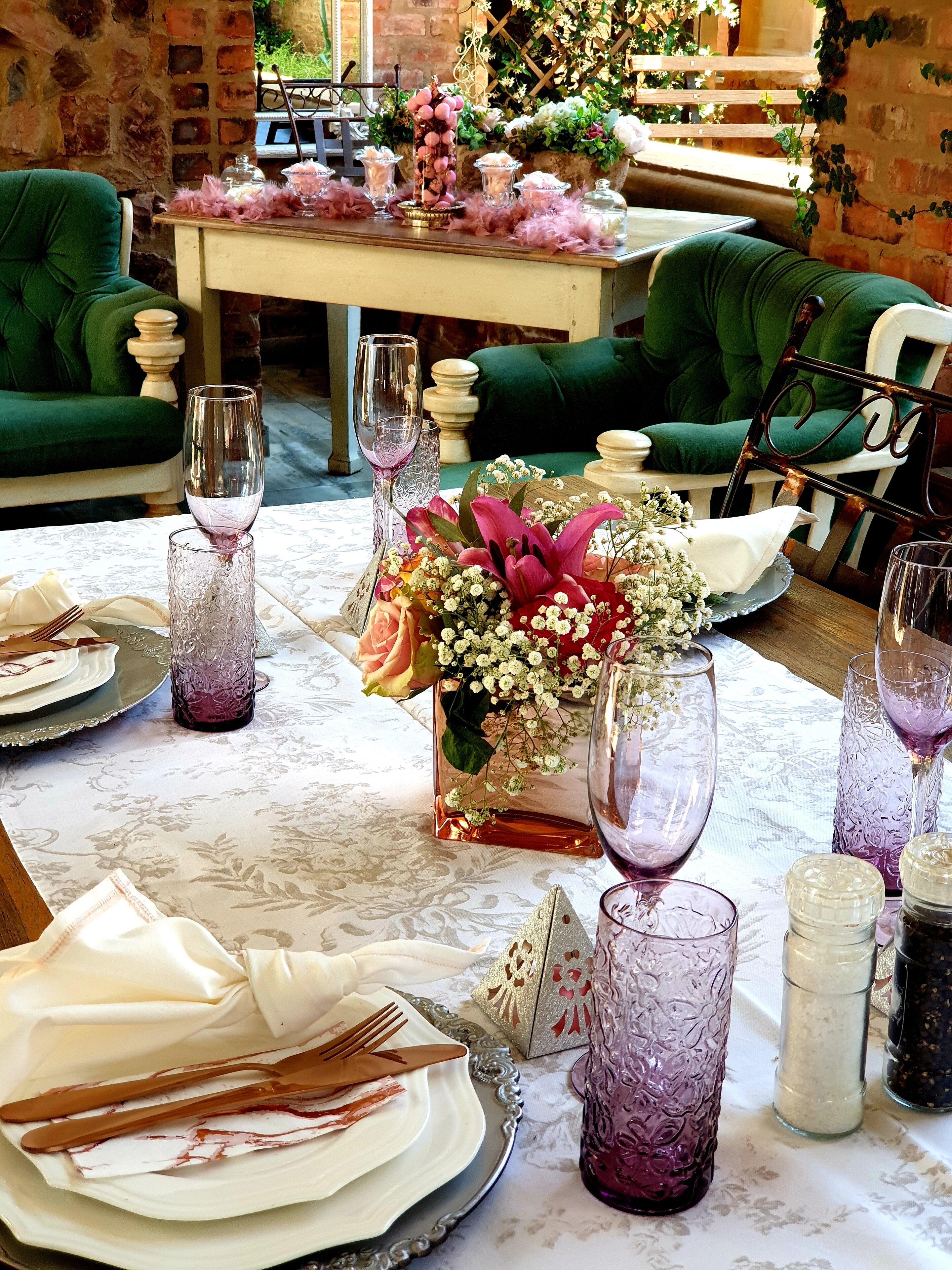 Un comedor con una mesa dispuesta para una comida, que incluye cristalería, platos y un centro de mesa con flores.
