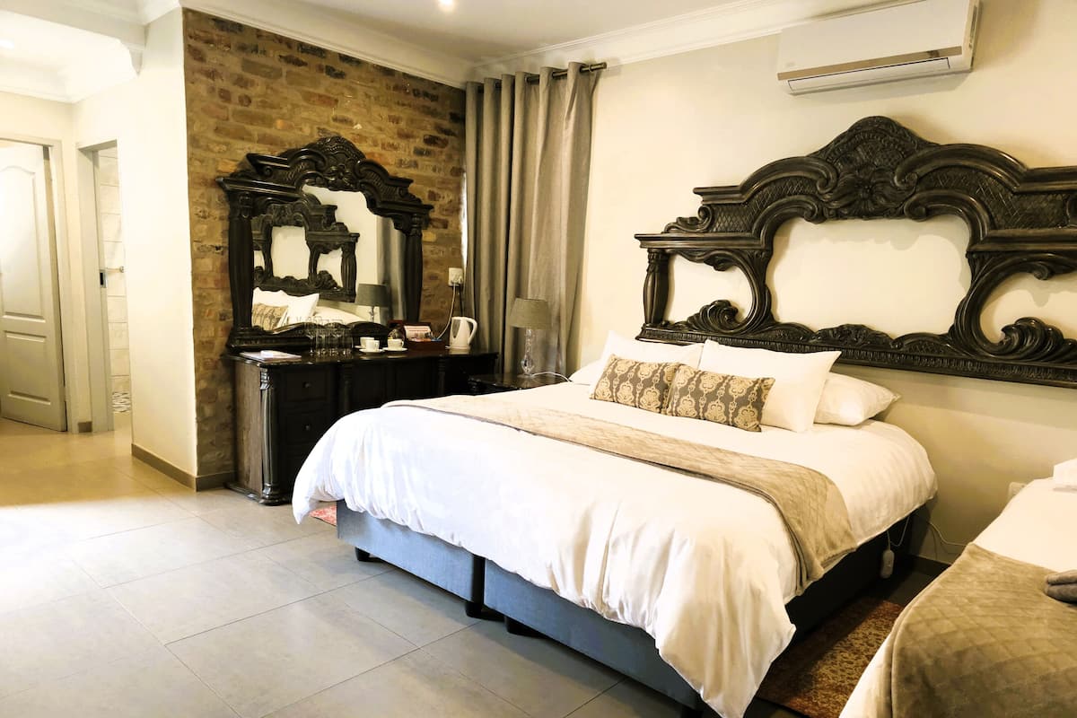 Une chambre avec un grand lit, une commode, un miroir et un mur en briques.