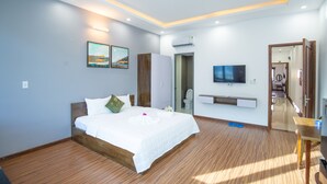 Moderni hotellihuone, jossa on puulattia, suuri sänky valkoisilla vuodevaatteilla, seinälle asennettu televisio ja pieni pöytä.