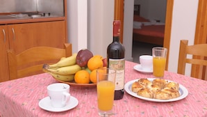 Une table de petit-déjeuner avec une bouteille de vin, un verre de jus d’orange, une assiette de viennoiseries, un bol de fruits et une tasse.
