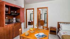 Une chambre d’hôtel compacte comprenant une table à manger en bois, un petit coin cuisine et un lit avec une tête de lit blanche.