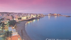 Une ville côtière au crépuscule, avec des bâtiments le long du front de mer, une jetée et une structure fortifiée sur une île.