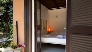 Een kamer met een bed, een bedlampje, een raam en uitzicht op groen.