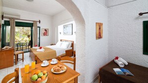 Ein Hotelzimmer mit Bett, Frühstückstisch mit Obst und Kaffee, einem Balkon mit Tisch und Stühlen und Blick ins Grüne.