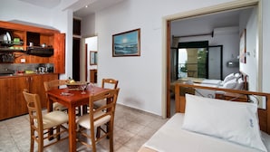 Quarto de hotel pequeno com mesa de jantar de madeira, cadeiras, cama com roupa de cama branca e vista para o mar pela janela.