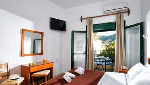 Quarto de hotel com cama, escrivaninha, cadeira, televisão e varanda com vista para as montanhas.
