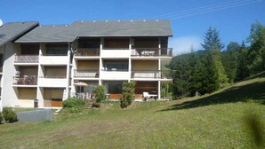 Um edifício com várias andares, varandas, um declive gramado e árvores ao fundo.