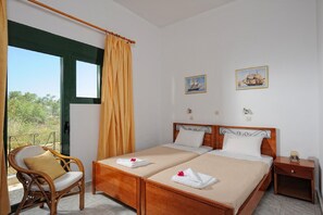 A double bed with two pillows, a wooden nightstand, a wicker chair, and a window with curtains. - Family 1 Bedroom Apt With Washing Machine (Hersonissos)