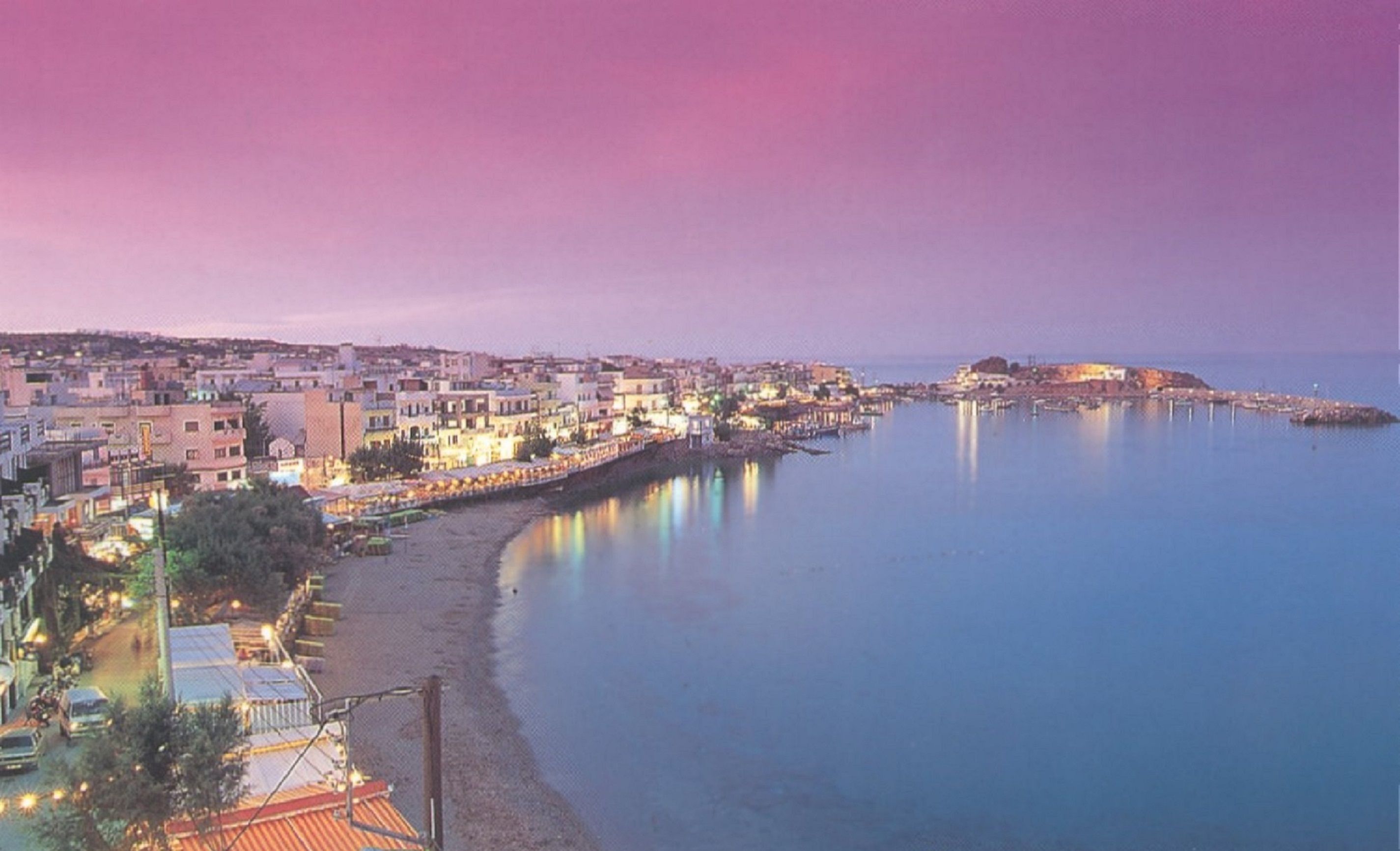 A coastal town at dusk with buildings along the waterfront and a clear view of the sea.