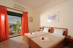 Quarto de hotel com duas camas, uma varanda com cortinas laranja, uma mesa e cadeiras do lado de fora e um quadro na parede.