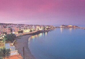 Un paysage urbain côtier au crépuscule, avec des bâtiments le long du front de mer, un ciel dégagé et une mer calme.