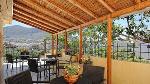 A covered patio with wicker furniture, a table with a basket of flowers, and a view of a mountainous landscape. - Charming Studio Near the Beach (Hersonissos)