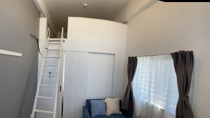 Ein kompakter Wohnraum mit Einbauschrank, einer Leiter zur Aufbewahrung, einer Couch mit Kissen und einem Fenster mit Vorhängen.