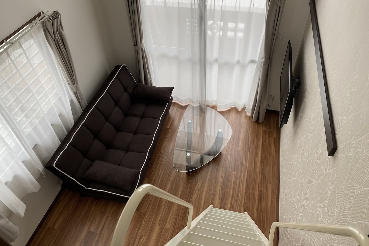 Una habitación moderna con un sofá marrón oscuro, una mesa de centro de cristal y una silla blanca.