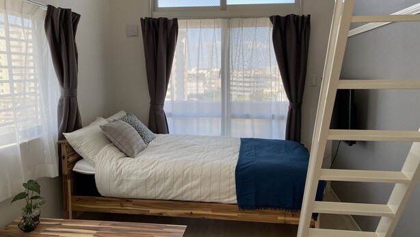 Ein Schlafzimmer mit einem Bett, Holzboden, einem Fenster mit Vorhängen und einer Leiter.