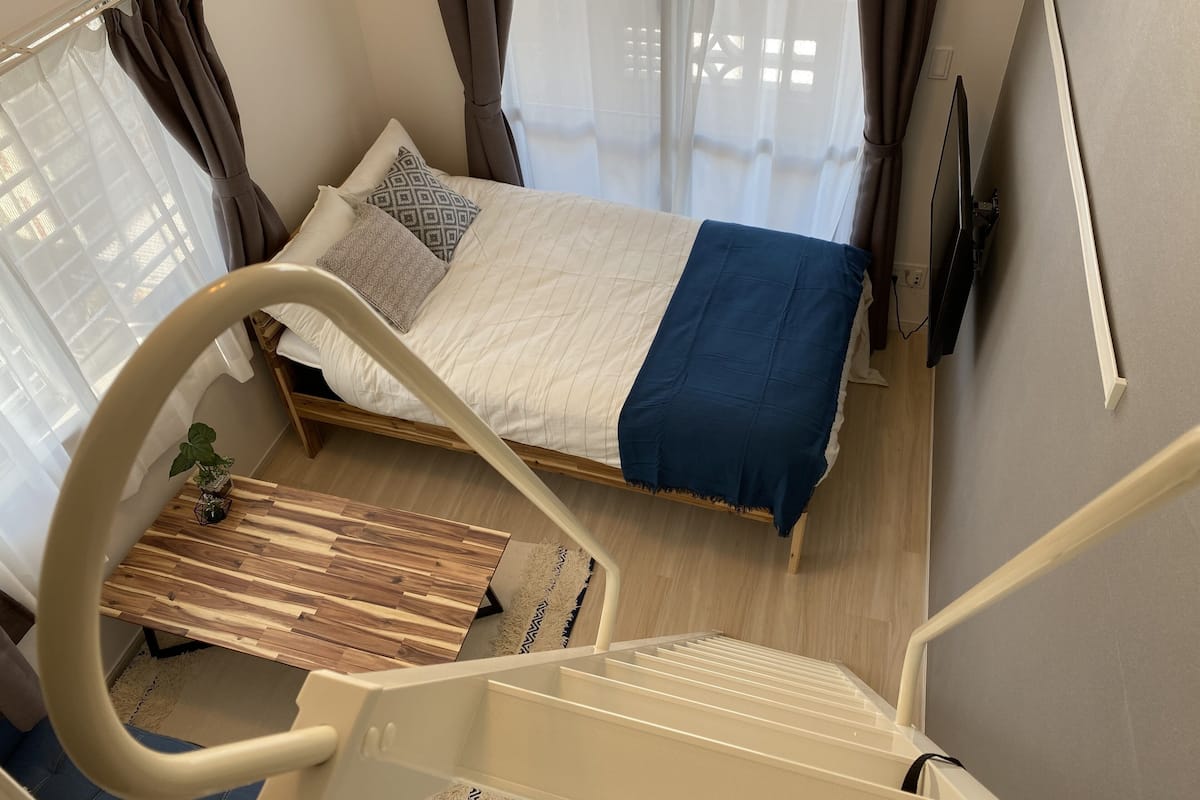 Un dormitorio con cama, televisor, piso de madera, ventana con cortinas y una escalera.