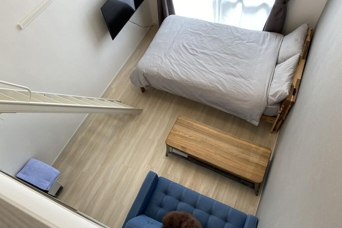 A bedroom with a bed, a wooden bench, a blue sofa, and a TV mounted on the wall.