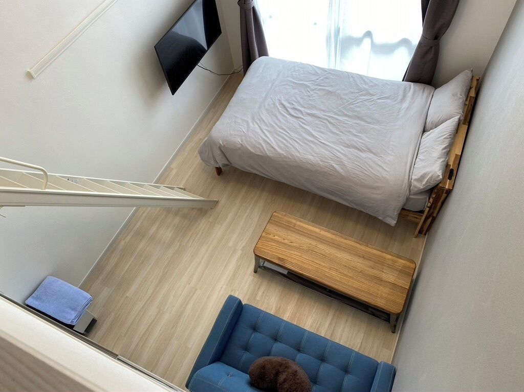 Una habitación con una cama, un sofá azul, un banco de madera y un televisor montado en la pared.