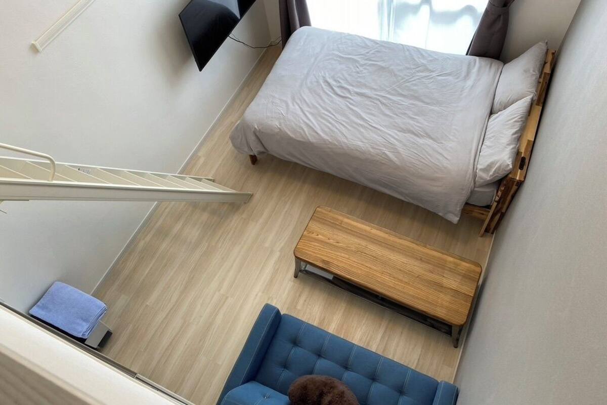 Una habitación con una cama, un sofá azul, un banco de madera y un televisor montado en la pared.