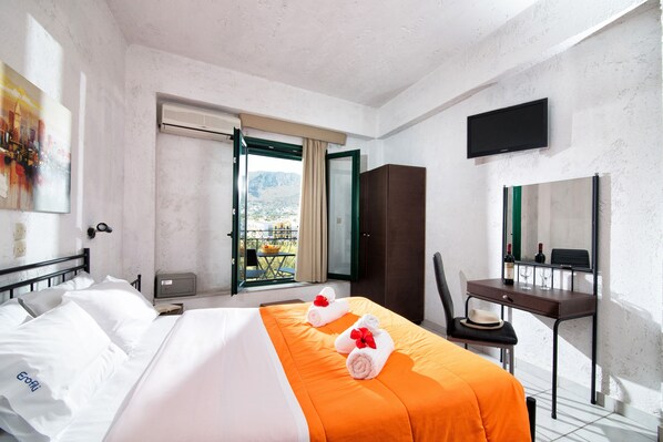 A hotel room with a bed, a desk, a chair, a television, and a window with a view of mountains. - Petite Studio Amazing Mountain View (Hersonissos)
