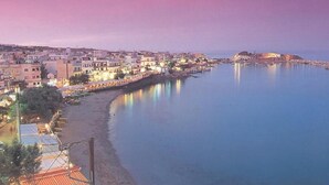 A coastal cityscape at dusk with buildings along the waterfront and a clear view of the sea.