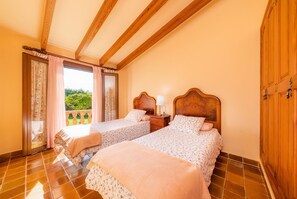 A bedroom with two beds, wooden beams, a balcony with curtains, and a view of greenery. - Rustic Holiday House Es Fasser with Pool, Garden, Terraces & Wi-Fi; Parking and Garage Available (Son Servera,)
