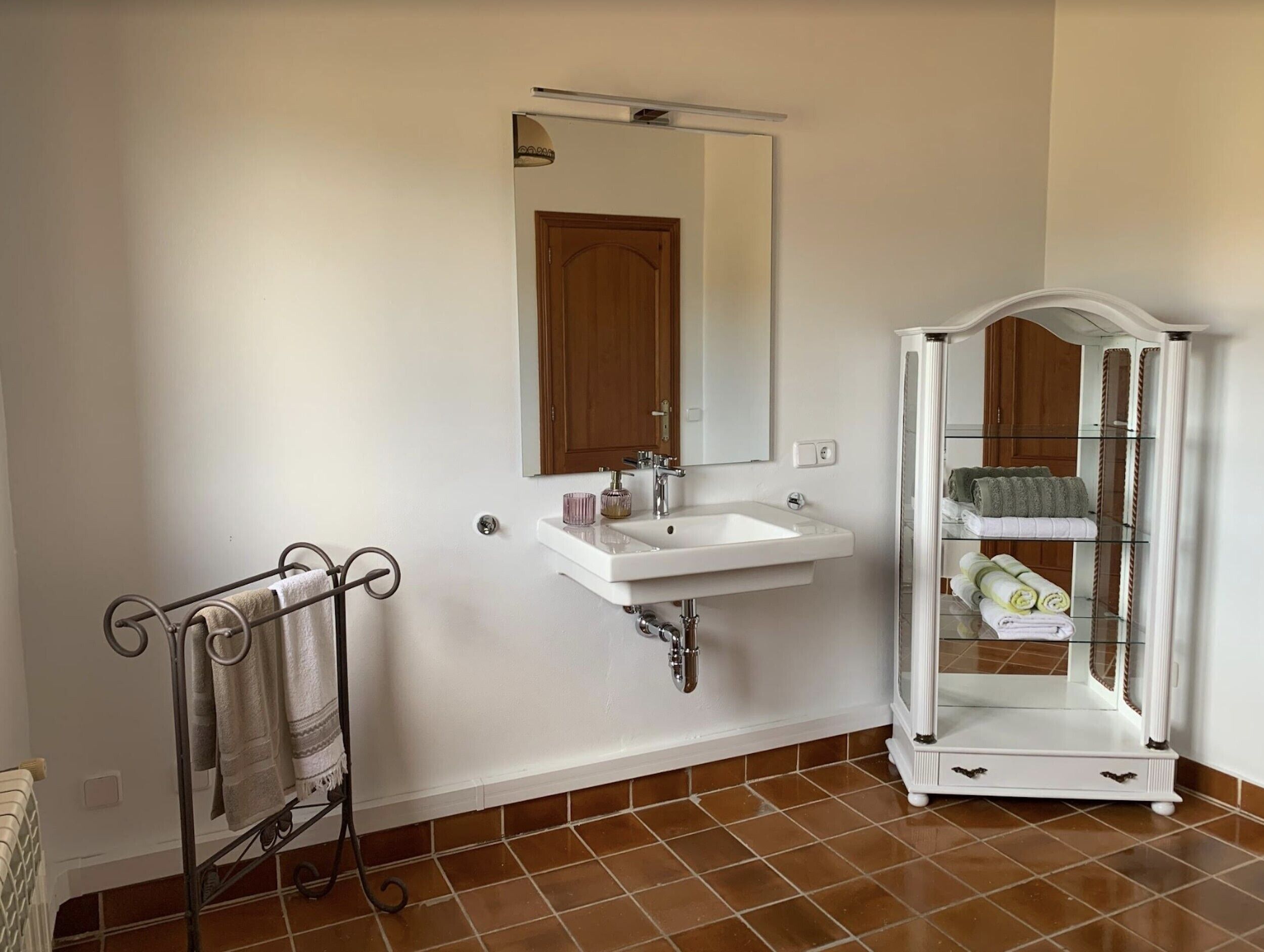 A bathroom with a white sink, a towel rack, a mirror, and a glass cabinet with towels.