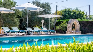 Ein Pool mit Liegestühlen und Sonnenschirmen, umgeben von Grünpflanzen und einem steinernen Bogen.