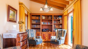 Ein Zimmer mit Holzboden, einer Kristallleuchter, einem Bücherregal, zwei gemusterten Sesseln, einem Holzschrank und einem Fliesenboden.