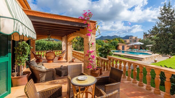 Eine Terrasse im Freien mit Korbmöbeln, einem Pool und Blick auf Berge.